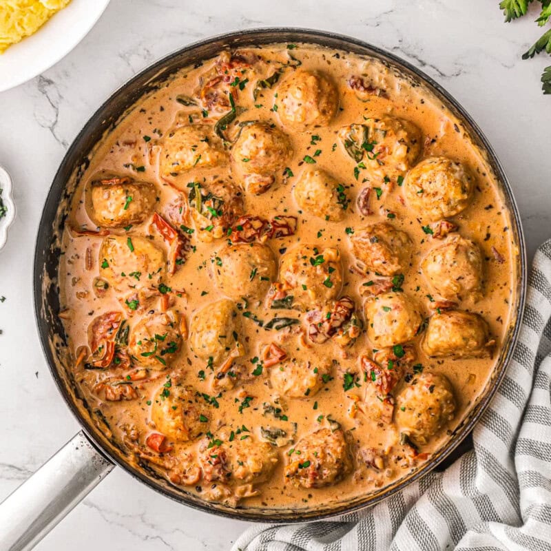 Marry me chicken meatballs in skillet with creamy sun dried tomato and Parmesan sauce. Mashed potatoes in bowl to the side.