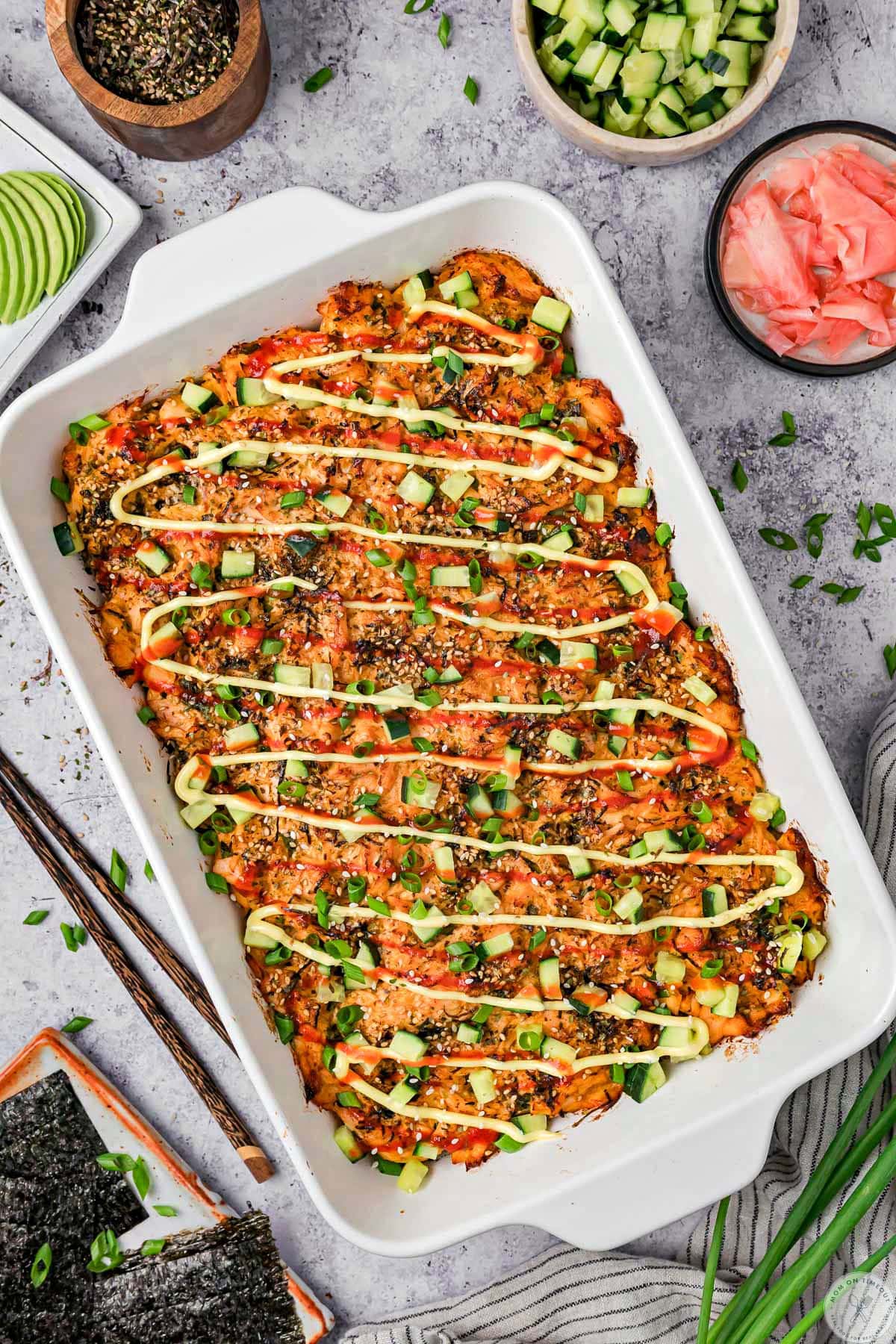 Overhead shot of salmon sushi bake in white casserole dish topped with sushi toppings.